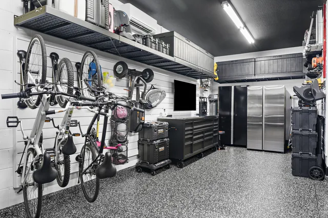 Overhead shelving extends above the slatwall and workbench, adding storage for bulky and seasonal items without taking space from the working area below.