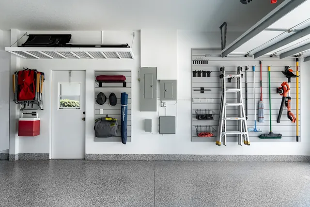 Wall storage groups outdoor gear beside the exterior door and long-handled tools farther along, keeping the doorway clear.