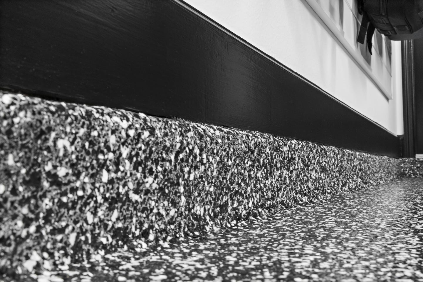 Close view of the textured floor coating and coated wall base beneath white slatwall