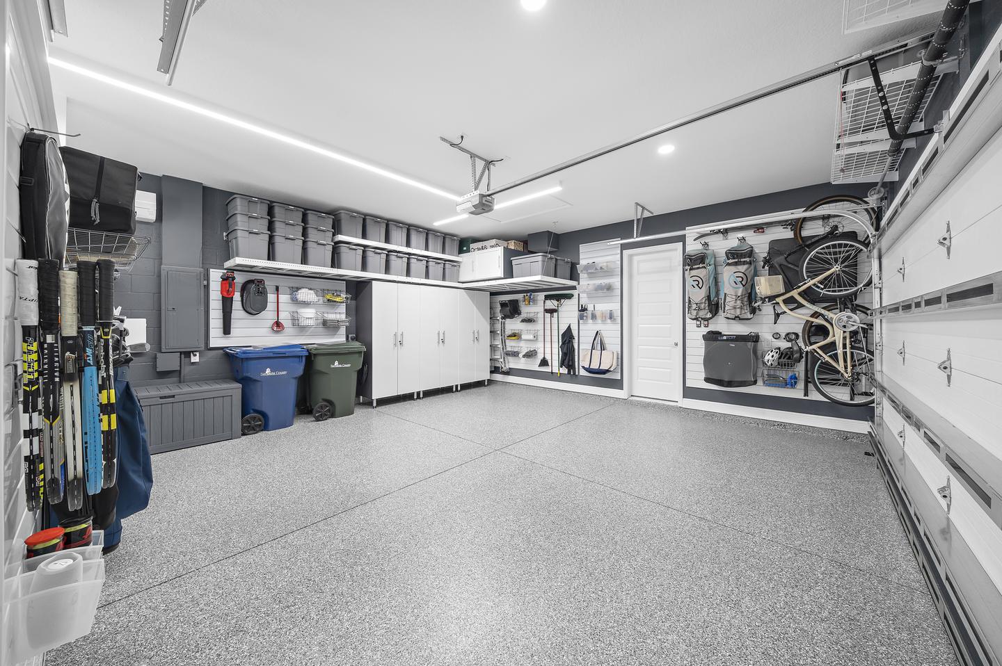Cabinetry, wall storage, and overhead bins organize household belongings around an open garage floor