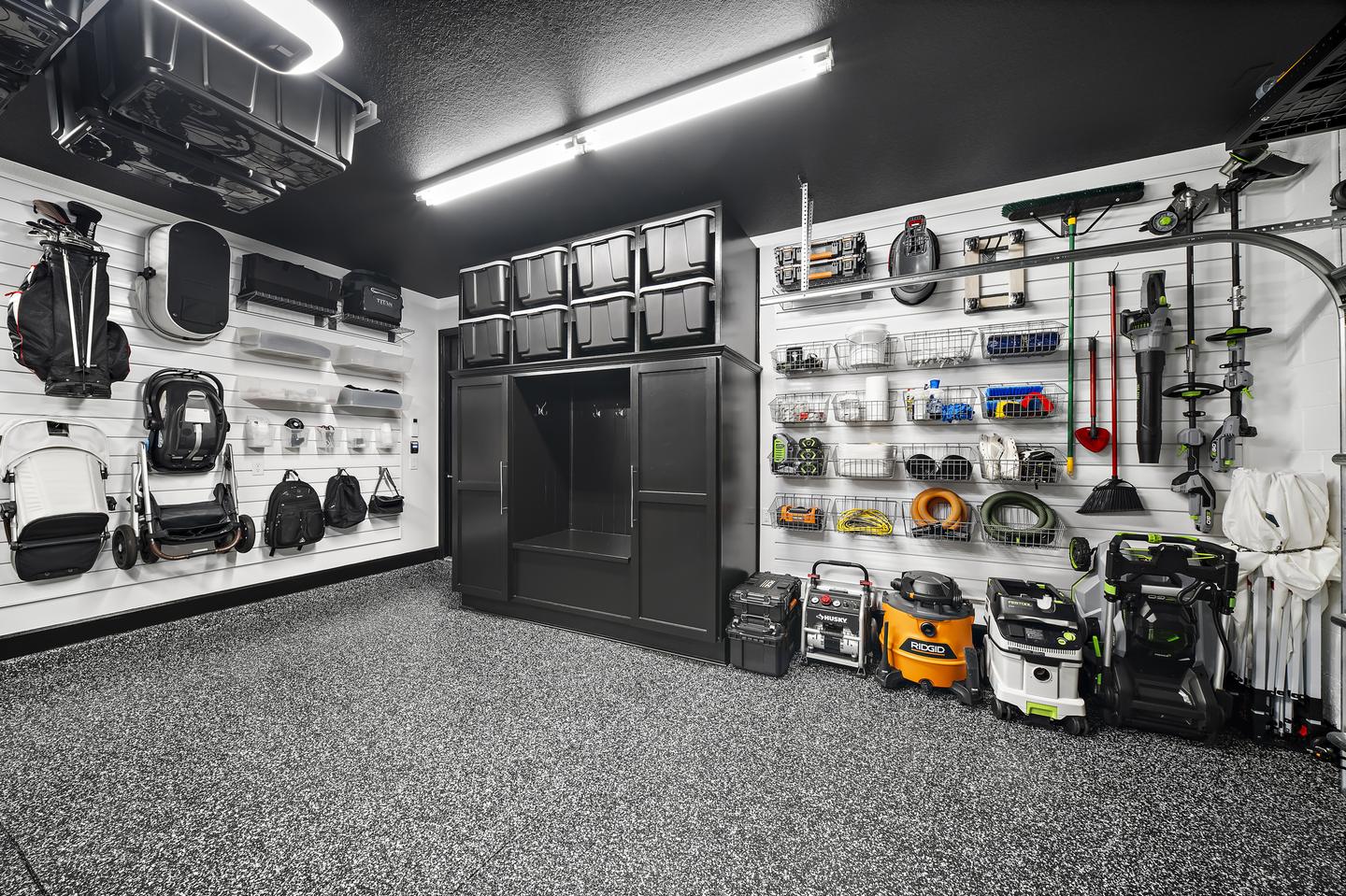 Tools, cleaning equipment, and household gear arranged on white slatwall around black cabinetry