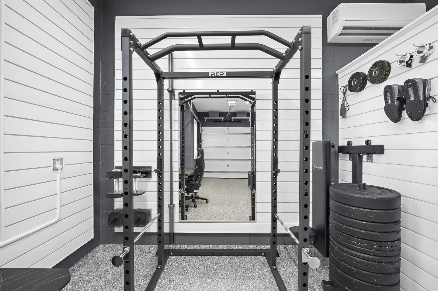 Exercise rack, mirror, and weights arranged within a garage fitness zone