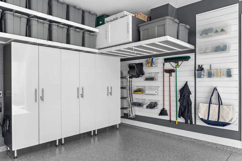 White cabinetry sits beneath overhead storage, with cleaning equipment and everyday essentials arranged on the adjoining slatwall.